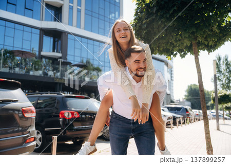 Woman is sitting on man, having fun. Happy couple together outdoors Woman is sitting on man, having fun. Happy couple together outdoors 137899257