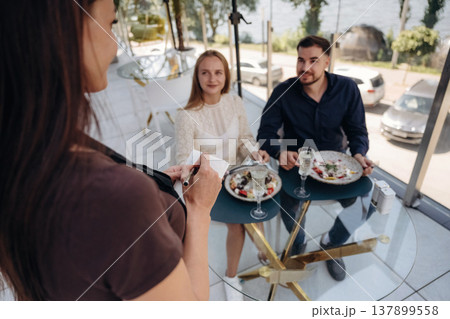 The waiter stands and takes the order. Couple enjoying date in the outdoor restaurant 137899558