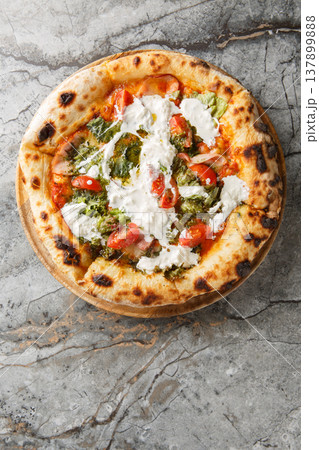 Italian Pizza with stracciatella cheese, pesto, ham and cherry tomatoes close-up on a wooden board. Vertical top view Italian Pizza with stracciatella cheese, pesto, ham and cherry tomatoes close-up on a wooden board. Vertical top view 137899888