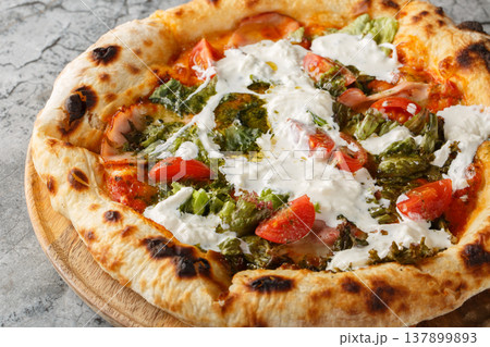 Close-up of neapolitan pizza with stracciatella cheese, pesto, ham and tomatoes on wooden board. Garnished with fresh thyme. Marble background 137899893