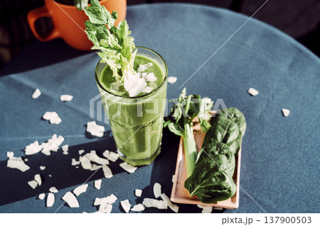 A healthy green smoothie made with fresh celery , standing on a table with a turquoise tablecloth. 137900503