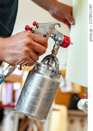Person holds a spray gun in a workshop for applying paint and finishing touches Person holds a spray gun in a workshop for applying paint and finishing touches 137901190