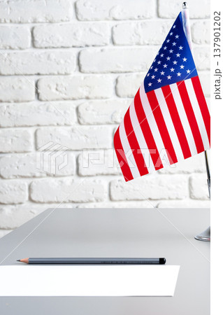Small USA flag on a desk with a pencil and blank paper in a simple room setting Small USA flag on a desk with a pencil and blank paper in a simple room setting 137901202