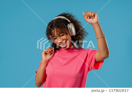 African Pretty Woman Listening Music, Dances With Wireless Headphones On Blue African Pretty Woman Listening Music, Dances With Wireless Headphones On Blue 137902657