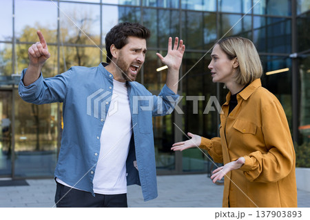 Angry man yelling and gesticulating during a heated argument with a woman in an urban setting, illustrating communication breakdowns and relationship stress Angry man yelling and gesticulating during a heated argument with a woman in an urban setting, illustrating communication breakdowns and relationship stress 137903893