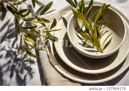 The table is set for a wedding with plates, folded linen napkins, and greenery as accents. Glasses of water sit next to each place setting in a bright indoor setting 137904178
