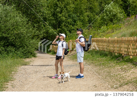 Active Man And Woman Hiking With Small Dog On Forest Trail During Summer Adventure 137904258
