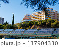 Solar panels and modern apartment buildings on a sunny day. Solar panels under residential buildings on a green hillside. Concept of renewable energy and sustainable architecture. 137904330