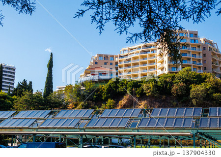 Solar panels and modern apartment buildings on a sunny day. Solar panels under residential buildings on a green hillside. Concept of renewable energy and sustainable architecture. Solar panels and modern apartment buildings on a sunny day. Solar panels under residential buildings on a green hillside. Concept of renewable energy and sustainable architecture. 137904330