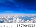 Aerial view of white fluffy clouds in deep blue sky. View from airplane above a sea of white fluffy clouds under rich blue sky. Calm travel cloudscape and freedom concept. 137904332