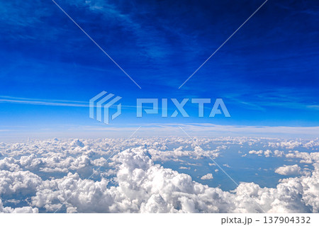 Aerial view of white fluffy clouds in deep blue sky. View from airplane above a sea of white fluffy clouds under rich blue sky. Calm travel cloudscape and freedom concept. Aerial view of white fluffy clouds in deep blue sky. View from airplane above a sea of white fluffy clouds under rich blue sky. Calm travel cloudscape and freedom concept. 137904332