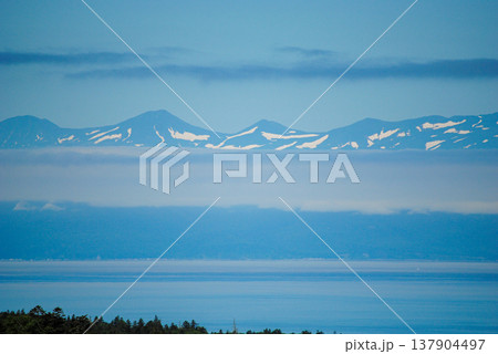 The photograph presents a stunning view of Hokkaido s snow-capped mountains from the coastline on a sunny summer day. The photograph presents a stunning view of Hokkaido s snow-capped mountains from the coastline on a sunny summer day. 137904497