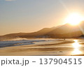 The sandy beach of a Kuril Islands bay glows beautifully at sunset on a sunny day. 137904515