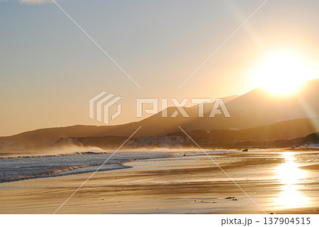 The sandy beach of a Kuril Islands bay glows beautifully at sunset on a sunny day. 137904515