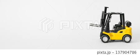 Forklift truck isolated on a blue background as a logic concept of warehouse storage. Conceptual photography showing a miniature toy loader symbolizing supply chain and logistics management with Forklift truck isolated on a blue background as a logic concept of warehouse storage. Conceptual photography showing a miniature toy loader symbolizing supply chain and logistics management with 137904786