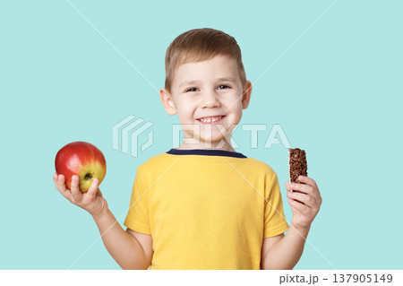 portrait of a little boy in a yellow t-shirt holding an apple and chocolate portrait of a little boy in a yellow t-shirt holding an apple and chocolate 137905149