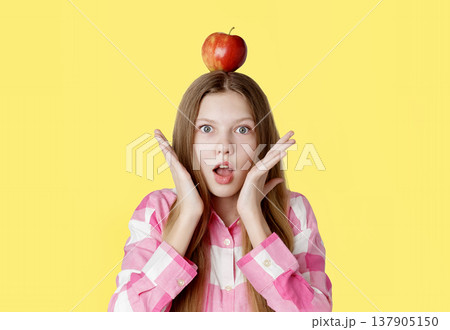 portrait of a young happy girl with an apple on her head, emotion of surprise from an idea portrait of a young happy girl with an apple on her head, emotion of surprise from an idea 137905150