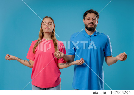 Calm young couple meditating together with closed eyes on blue studio background Calm young couple meditating together with closed eyes on blue studio background 137905204