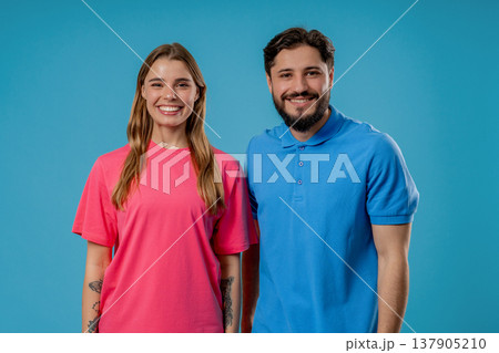 Happy young couple smiling at camera standing together on blue studio background Happy young couple smiling at camera standing together on blue studio background 137905210
