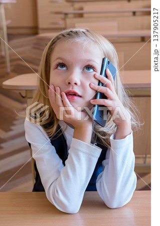 A first grade student at school speaks by phone. emotions of schoolgirls A first grade student at school speaks by phone. emotions of schoolgirls 137905217