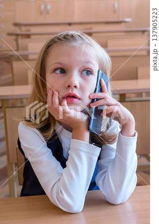 A first grade student at school speaks by phone. emotions of schoolgirls A first grade student at school speaks by phone. emotions of schoolgirls 137905223