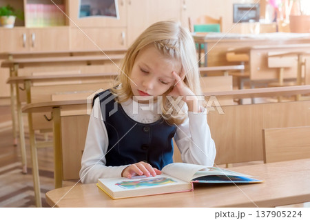 girl in the first grade, is sitting at the desk with book girl in the first grade, is sitting at the desk with book 137905224