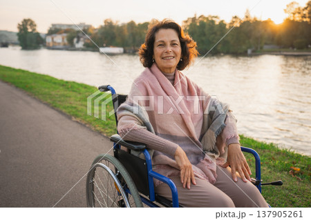 Happy senior woman in wheelchair smiling enjoying freedom walking on road in city park outdoor. Old cheerful positive woman in chair for people with disability. Disability disease rehabilitation 137905261