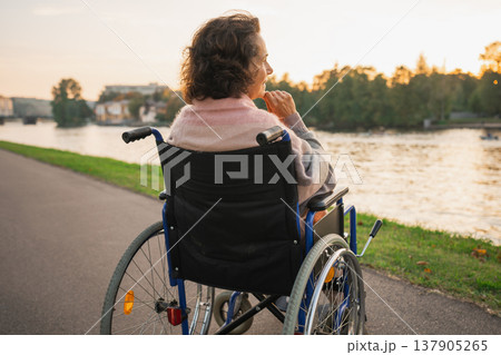 Sad senior woman sitting in wheelchair walking on road in city outdoor, back view. Old paralyzed lady in chair for people with disability feel depressed. Lonely elderly sick woman sits on wheelchair Sad senior woman sitting in wheelchair walking on road in city outdoor, back view. Old paralyzed lady in chair for people with disability feel depressed. Lonely elderly sick woman sits on wheelchair 137905265