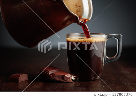 Black coffee is poured into a glass cup. 137905370
