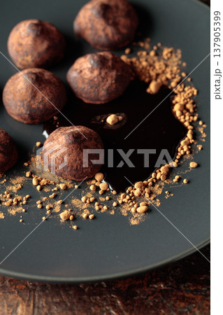 Chocolate truffles with cocoa powder and chocolate sauce on a black plate. 137905399