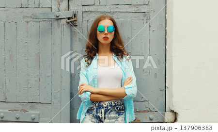 Portrait of stylish modern young woman in glasses, shorts posing on urban wall background Portrait of stylish modern young woman in glasses, shorts posing on urban wall background 137906388