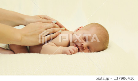 Mother gives massage to sleeping baby lying on the bed on white background, child and health concept Mother gives massage to sleeping baby lying on the bed on white background, child and health concept 137906410