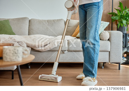 Woman vacuuming floor with cordless vacuum cleaner in living room near sofa Woman vacuuming floor with cordless vacuum cleaner in living room near sofa 137906981