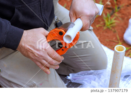 Hands work with pipe cutter to prepare plastic tubing in garden setting 137907179