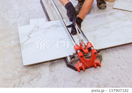 Worker uses tile cutter to cut large tiles for flooring in indoor area home renovation process 137907182