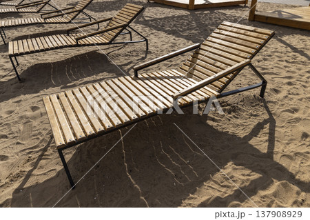 empty wooden sun beds on the sandy beach after the end of the season, empty sun beds on the beach at the beginning of autumn in Europe in cold weather 137908929