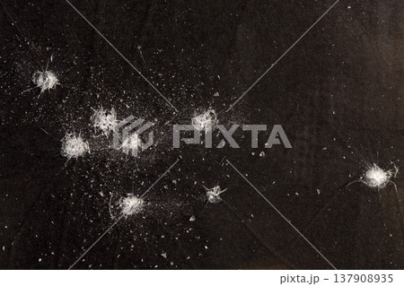thin broken glass on black paper, dents and dots on the glass where it broke, white cracks and completely broken places on the glass on a black uneven background 137908935