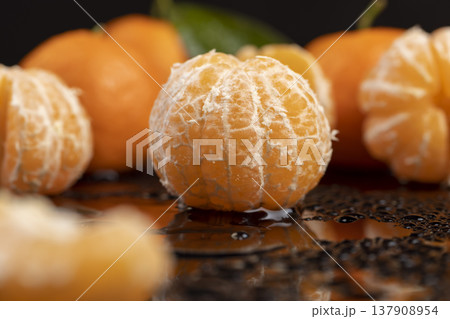 ripe orange and juicy and peeled tangerines lie on a black surface covered with clear drops of water, fresh soft and sweet tangerines on a black glass covered with a large number of drops of water ripe orange and juicy and peeled tangerines lie on a black surface covered with clear drops of water, fresh soft and sweet tangerines on a black glass covered with a large number of drops of water 137908954