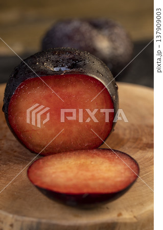 sliced fresh juicy plums on the kitchen table, some beautiful pure black plums on the table, plum with red juicy sweet flesh cut into pieces 137909003
