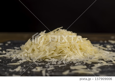 hard ripe cheese grated into small pieces for cooking pasta or pizza, grated piece of yellow cheese as an ingredient for a large dish, close up 137909006