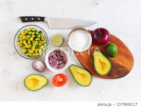 Avocado halves, limes and onions - basic guacamole ingredients on white working board, knife above, flat lay photo Avocado halves, limes and onions - basic guacamole ingredients on white working board, knife above, flat lay photo 137909217