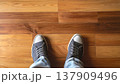 木目のフローリングに立つスニーカーの足元と室内の温かみ 137909496