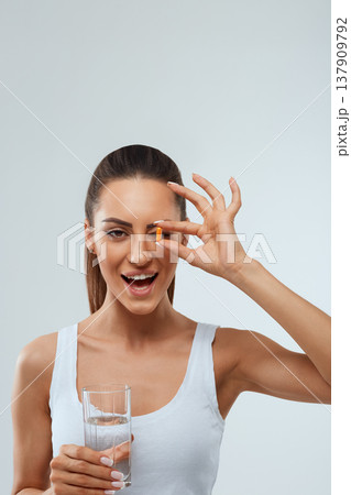 Portrait of beautiful woman holding glass of fresh water. Smiling girl taking omega 3 fish oil capsule, Portrait of beautiful woman holding glass of fresh water. Smiling girl taking omega 3 fish oil capsule, 137909792