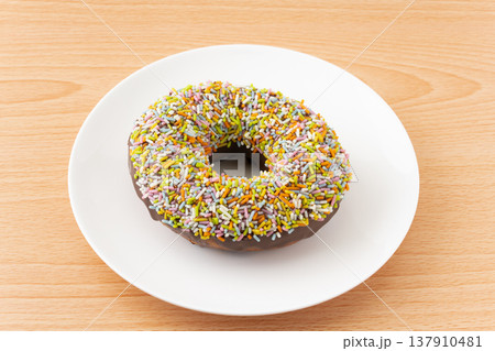 お皿に載せたカラースプレーをまぶした1個のチョコドーナツ 137910481