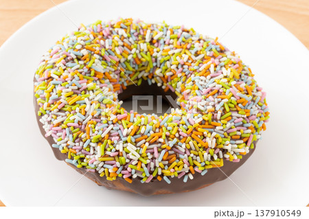 お皿に載せたカラースプレーをまぶしたチョコドーナツのクローズアップ 137910549