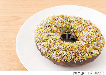 お皿に載せたカラースプレーをまぶしたチョコドーナツのクローズアップ お皿に載せたカラースプレーをまぶしたチョコドーナツのクローズアップ 137910550