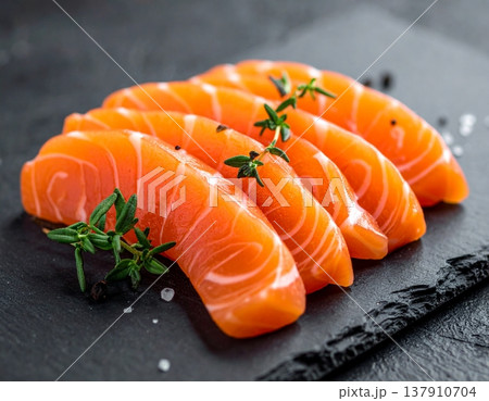 Salmon slices sashimi with thyme on a rustic slate platter against a dark backdrop Salmon slices sashimi with thyme on a rustic slate platter against a dark backdrop 137910704
