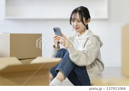 段ボール箱に囲まれて座わりスマートフォンを見る若い女性 引っ越し イメージ 段ボール箱に囲まれて座わりスマートフォンを見る若い女性 引っ越し イメージ 137911066
