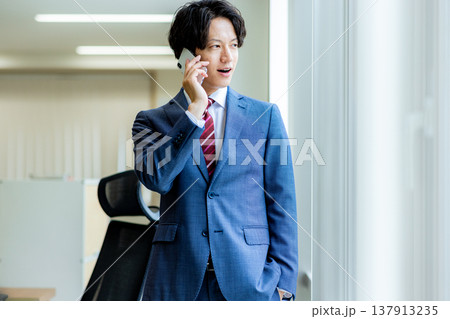 オフィスでスマホで電話をする若いビジネスマン オフィスでスマホで電話をする若いビジネスマン 137913235
