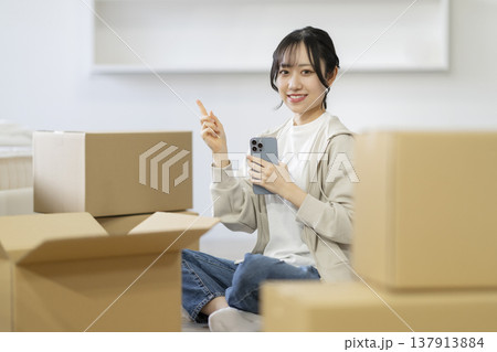 段ボール箱に囲まれて座る笑顔の若い女性 (指1本のポーズ) カメラ目線 引っ越し イメージ 段ボール箱に囲まれて座る笑顔の若い女性 (指1本のポーズ) カメラ目線 引っ越し イメージ 137913884